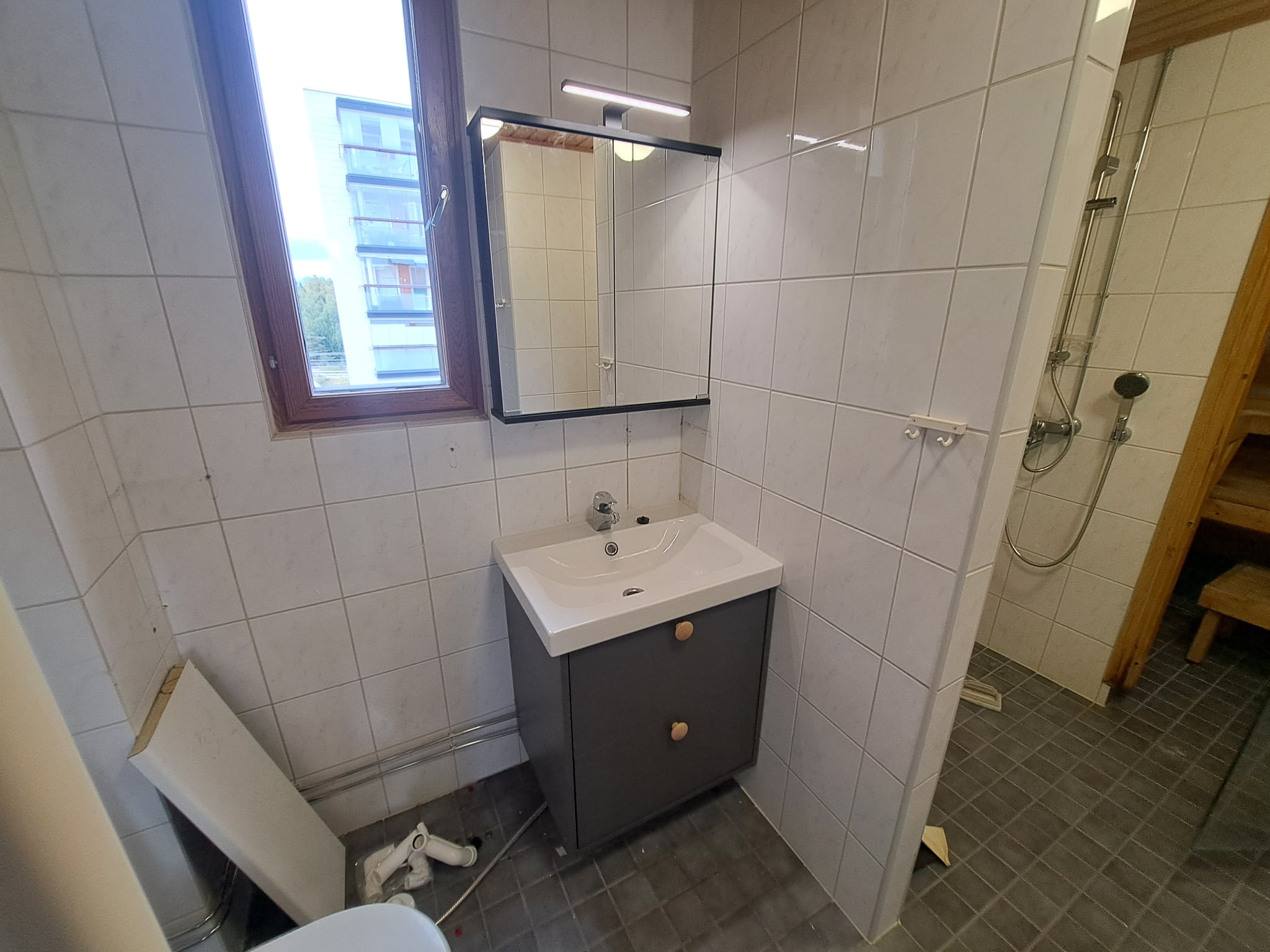 Remontoitu kylpyhuone, jossa on allaskaappi, peili ja vaaleat seinälaatat.