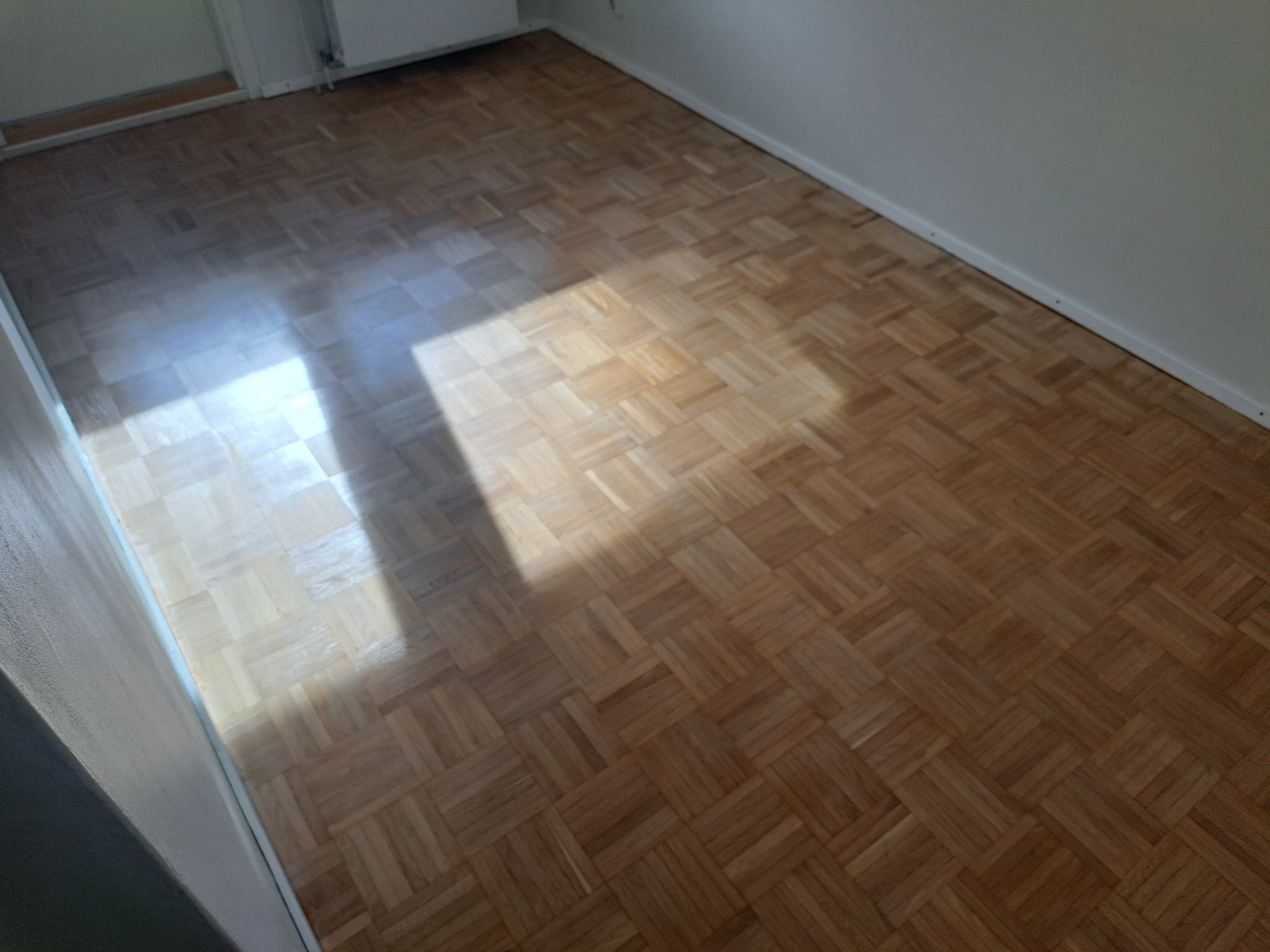 Finished parquet wood flooring with a natural oak finish and sunlight highlighting the wood pattern
