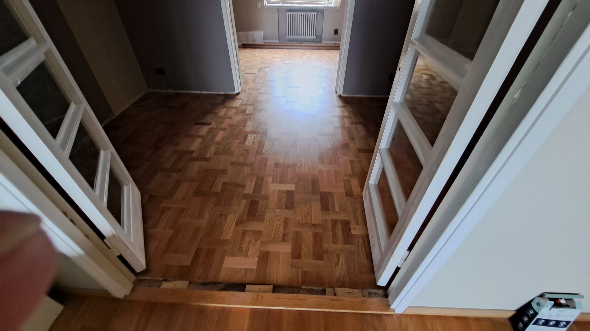  Kunnostettu mosaiikkiparketti ja puiset lattialistat asunnon huoneessa, jossa on valkoiset lasiovet.