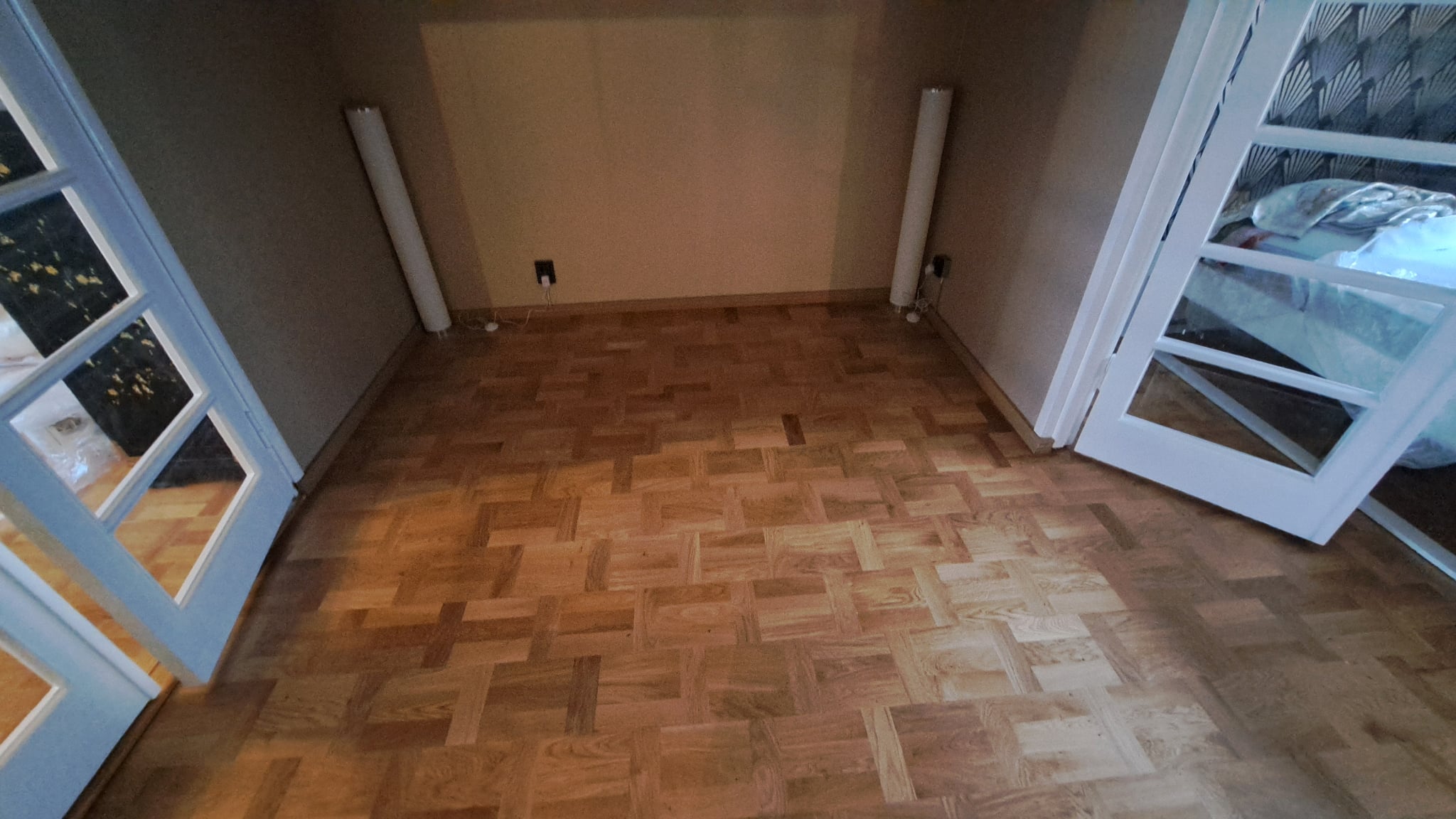 Kunnostettu puinen mosaiikkiparketti ja valkoiset lasiovet lattian korjaustyön jälkeen.