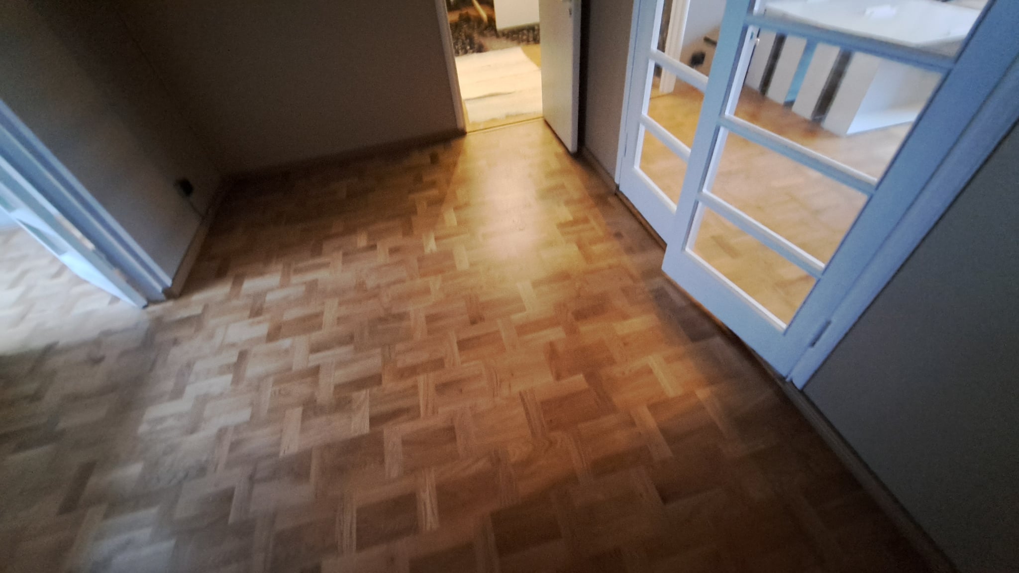 Vaalea mosaiikkiparketti asennettuna ja viimeisteltynä huoneessa, jossa on suuret lasiovet ja luonnonvaloa.