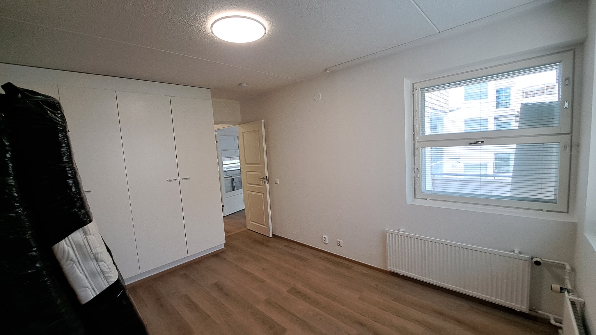 Huoneen pintaremontti Helsingissä, jossa on valkoiset seinät, puunsävyinen lattia ja suuri ikkuna.