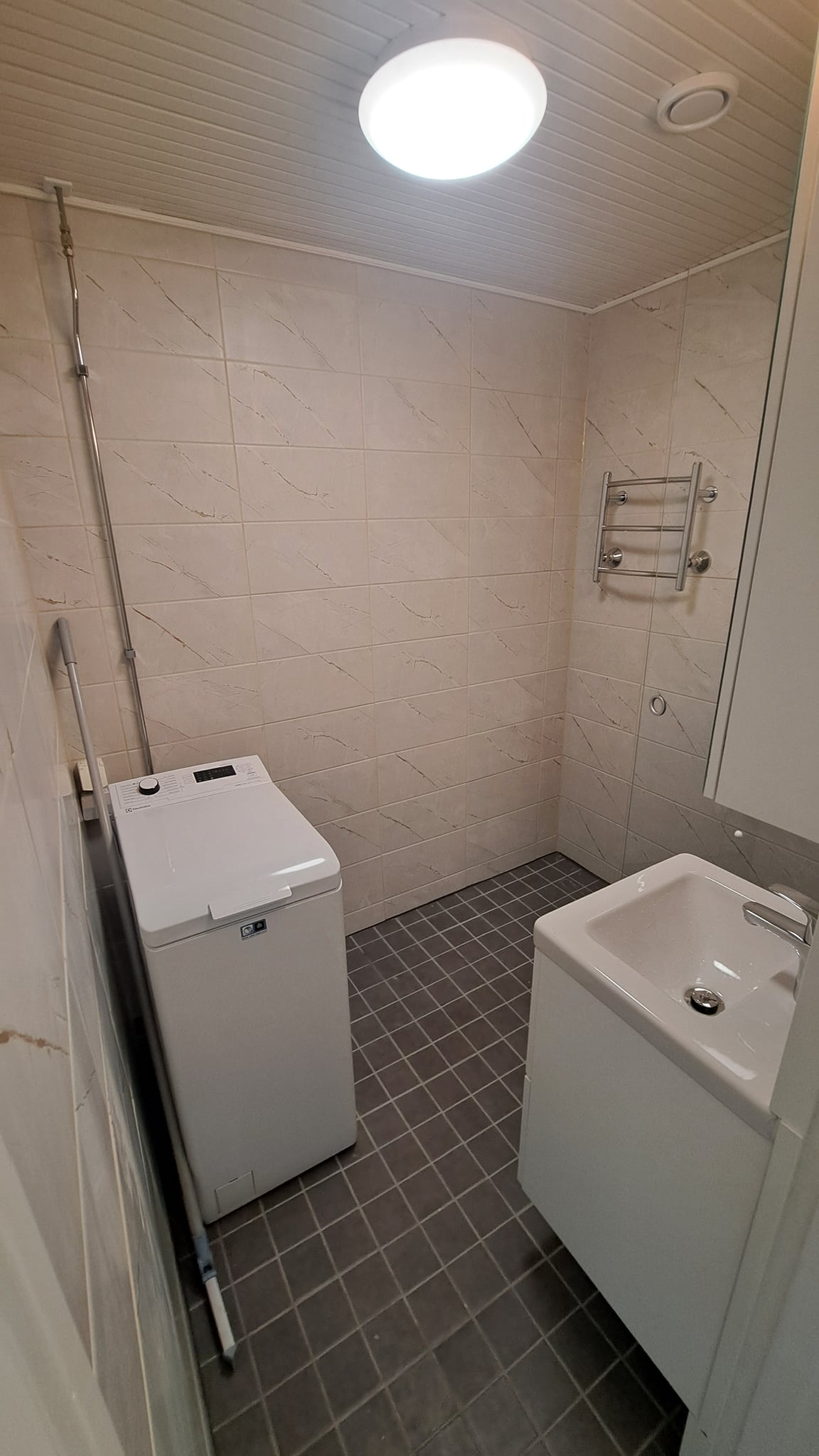 Pieni remontoitu kylpyhuone Helsingissä, jossa on wc-istuin, vaaleat seinät ja tummat lattialaatat.