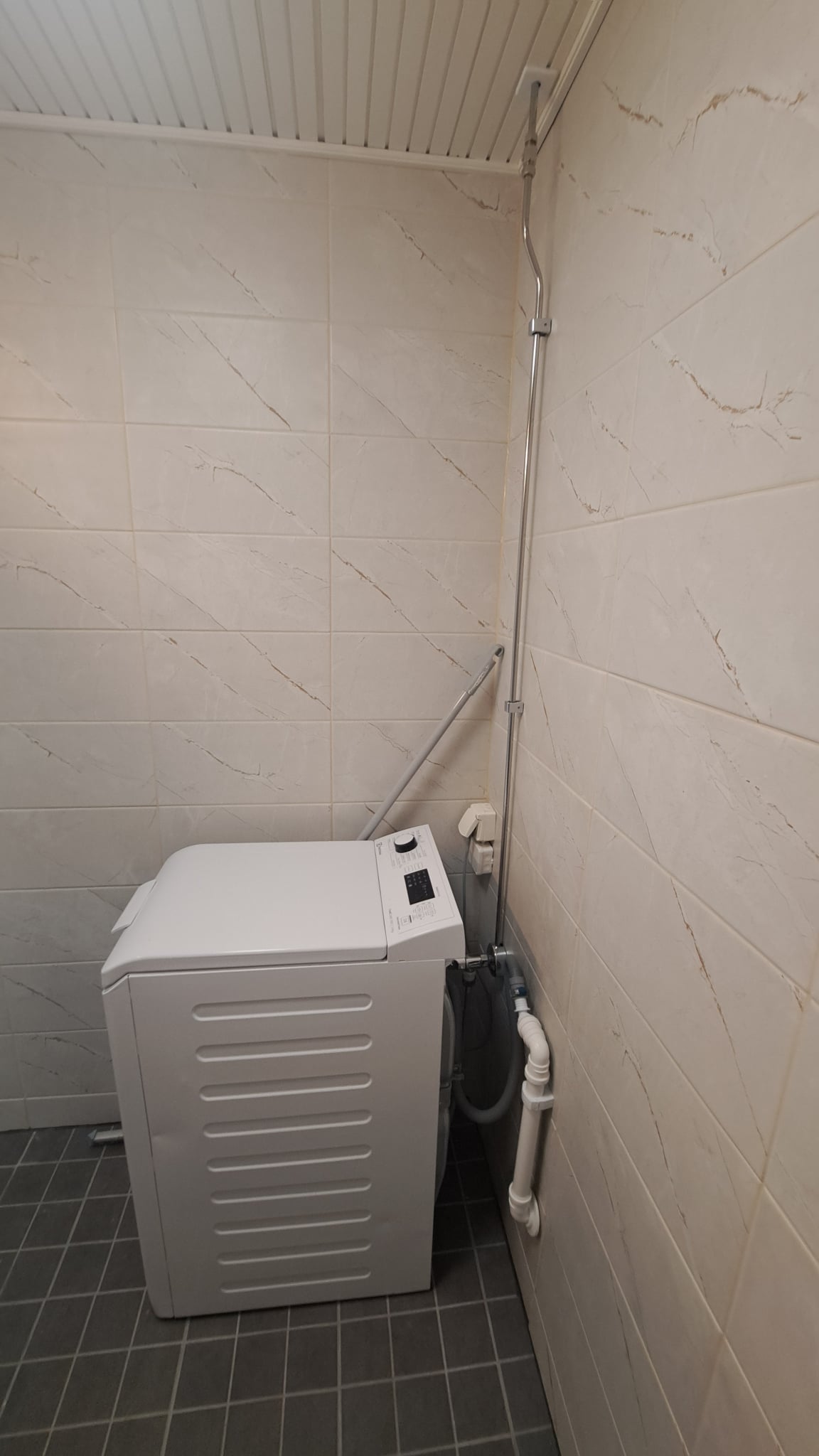 Remontoidun kylpyhuoneen nurkkaus Helsingissä, jossa on valkoinen pyykinpesukone ja tummat lattialaatat.
