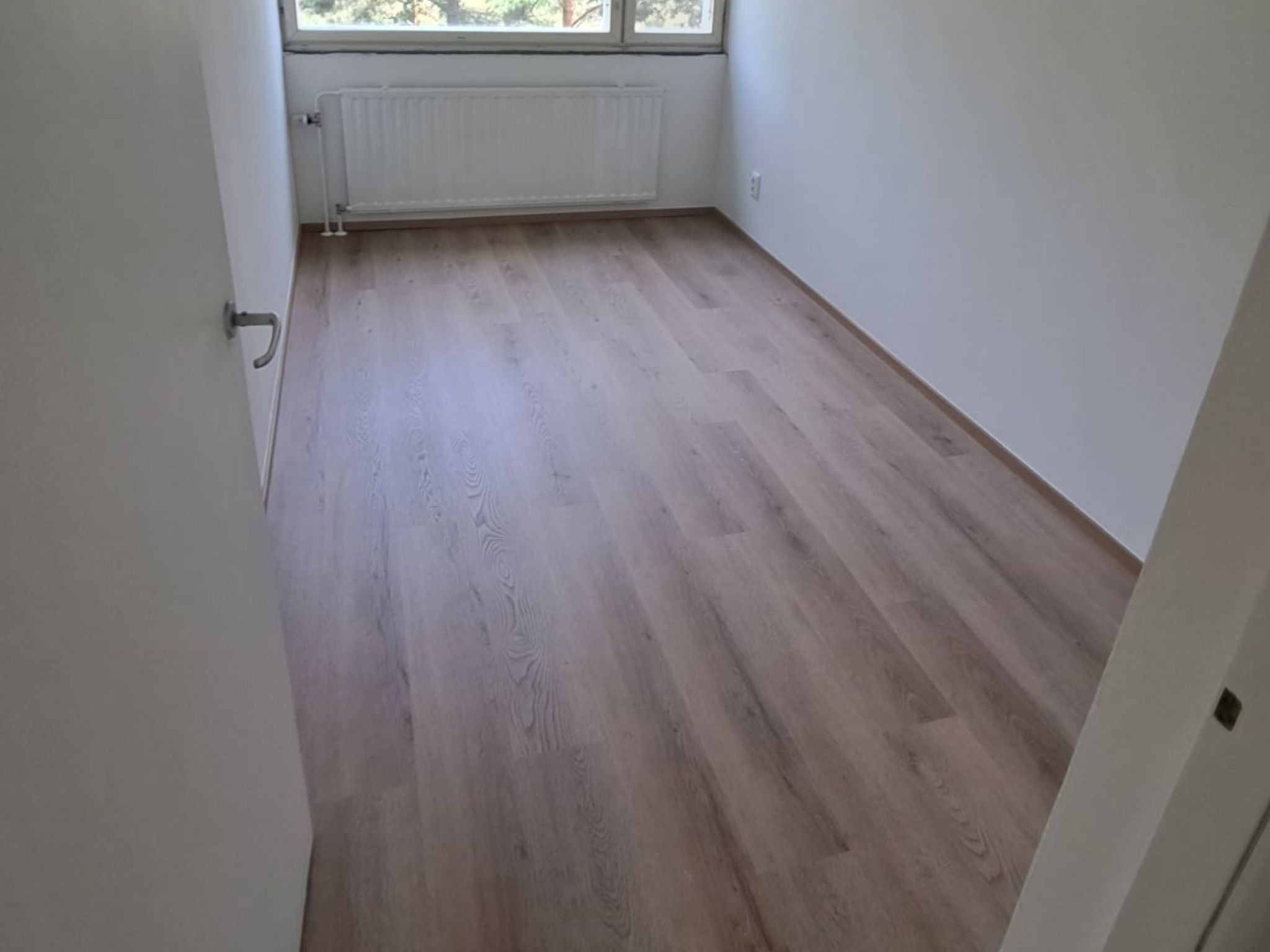 Huone Helsingissä, jossa on uusi puunsävyinen lattia ja vaaleat seinät.