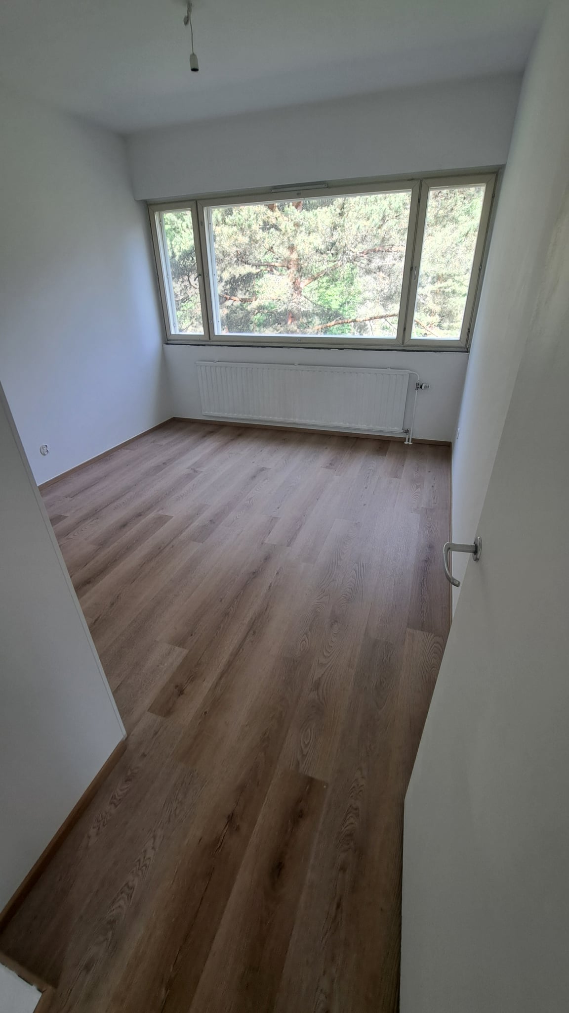 Huoneen uusi puunsävyinen lattia Helsingissä, luonnonvaloa tuovan ikkunan alla.
