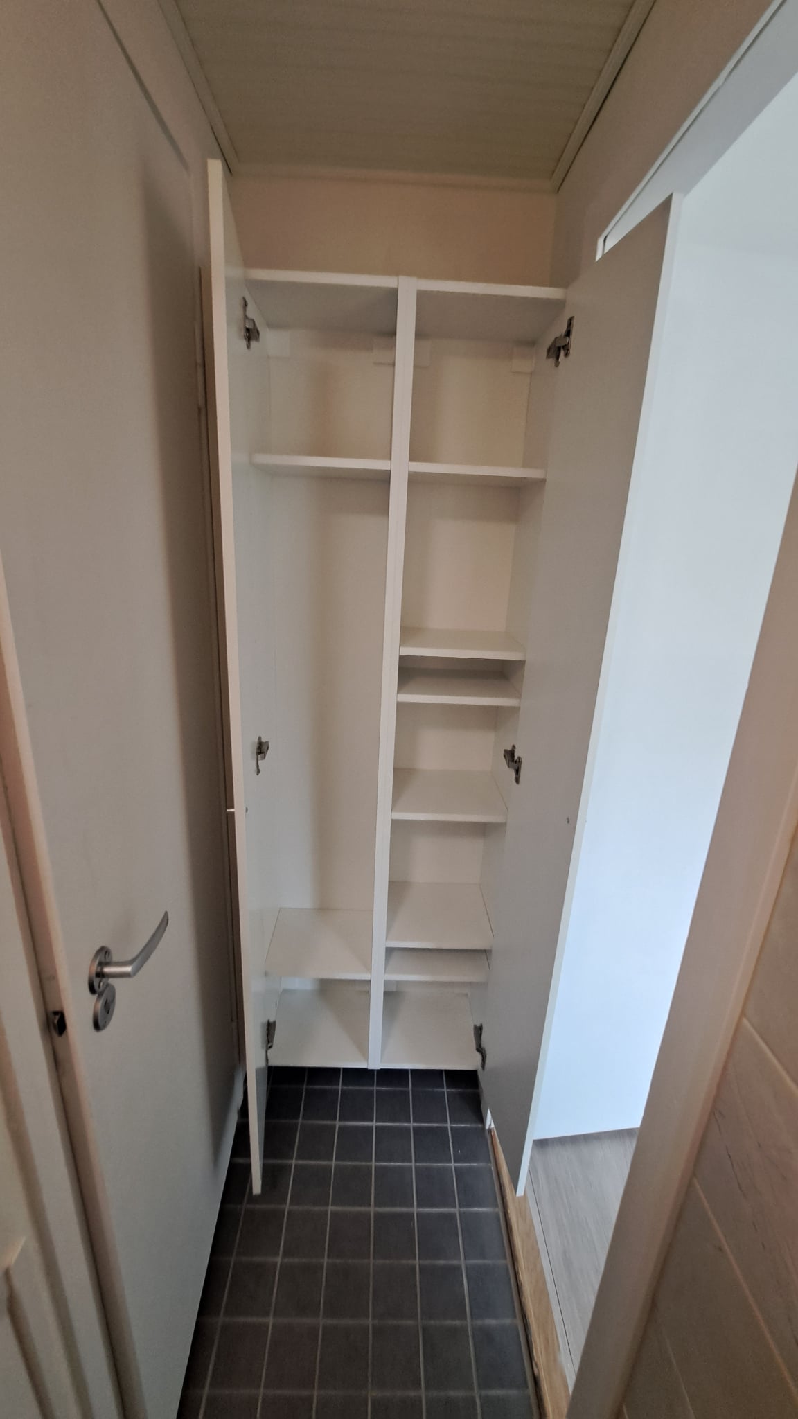 Kunnostettu eteinen Helsingissä, jossa on avohyllyt, vaaleat seinät ja tummat lattialaatat.